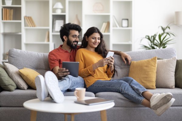 Happy Young Couple Relaxing At Home With Smartphone And Digital Tablet WiFi Setup Whole-Home Coverage